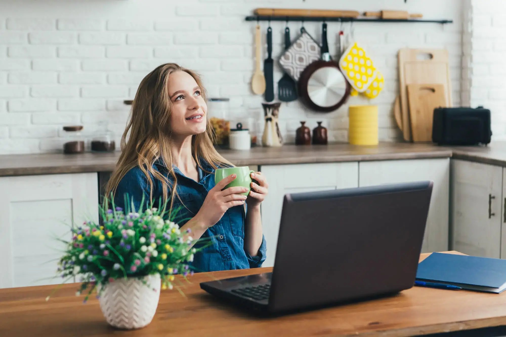 Mujer joven, sentada frente a una computadora, sosteniendo una taza de café y con una mirada reflexiva