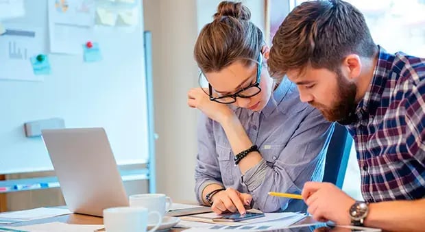Pareja sentada en una oficina revisando documentos financieros con calculadora y computadora portátil, analizando presupuesto o deudas.