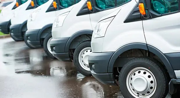 Fila de vehículos utilitarios blancos estacionados sobre pavimento mojado, representando una flota comercial o empresarial.
