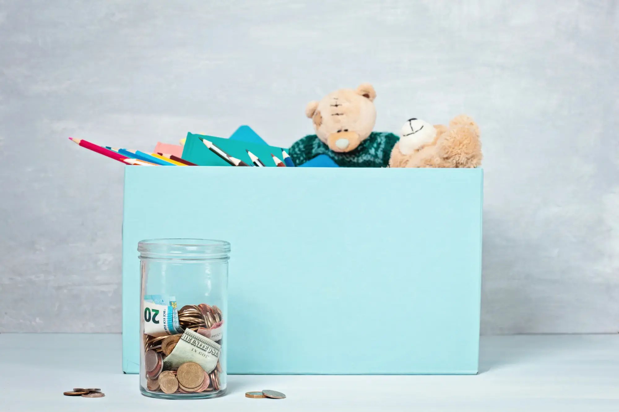 Caja azul con peluches, útiles escolares y frasco con monedas delante