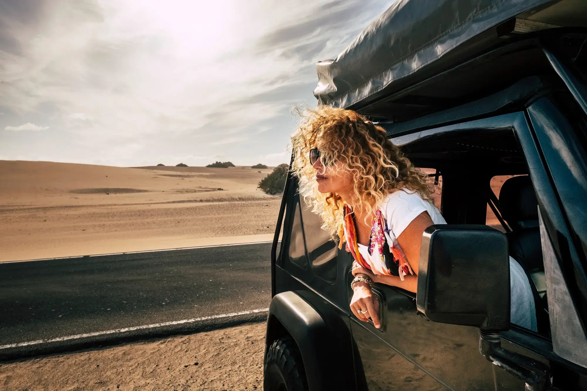 Mujer disfrutando de un viaje por carretera en el desierto, asomada por la ventana de su vehículo.