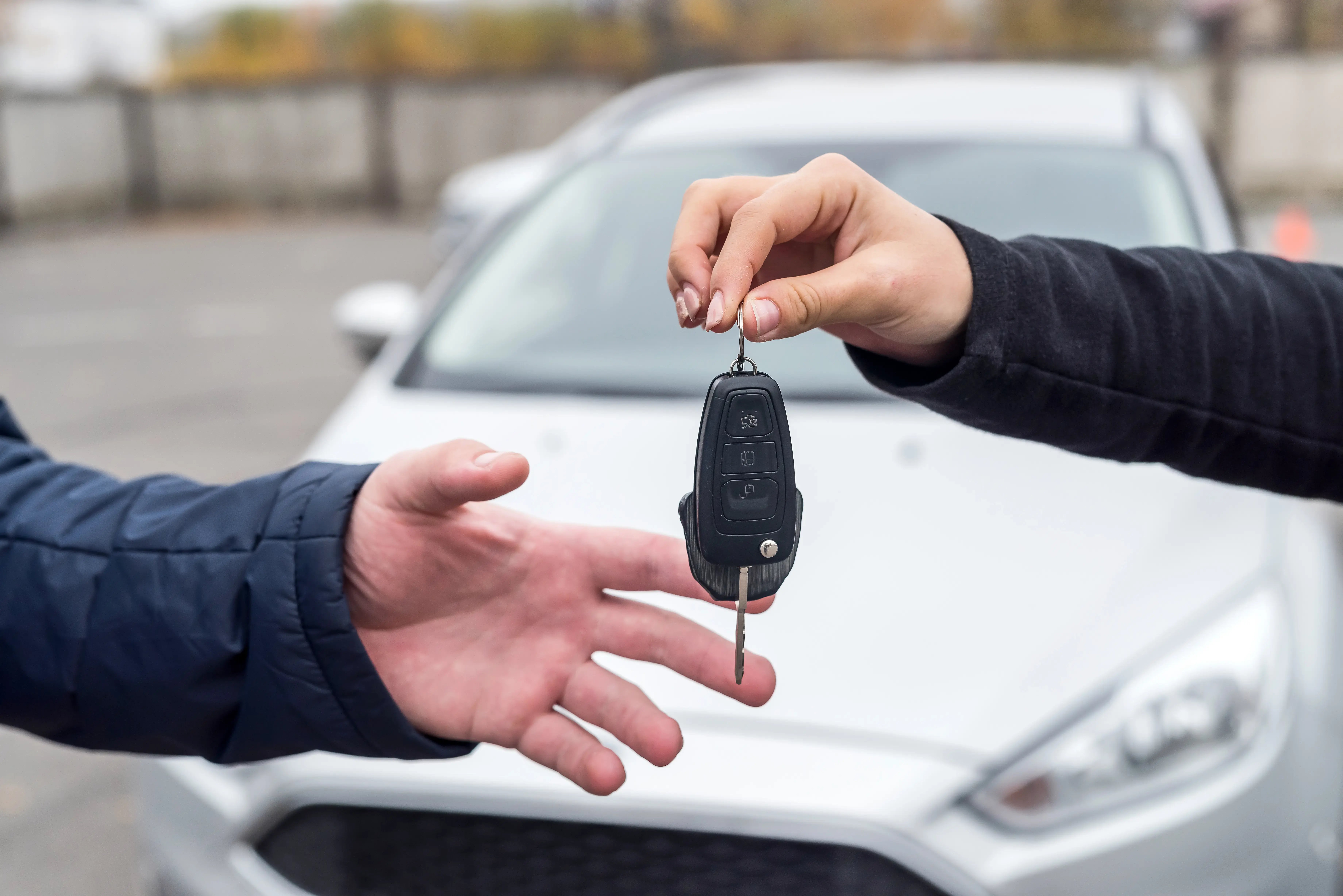 Persona entregando una llave de automóvil a otra frente a un vehículo estacionado, representando la compra o alquiler de un auto