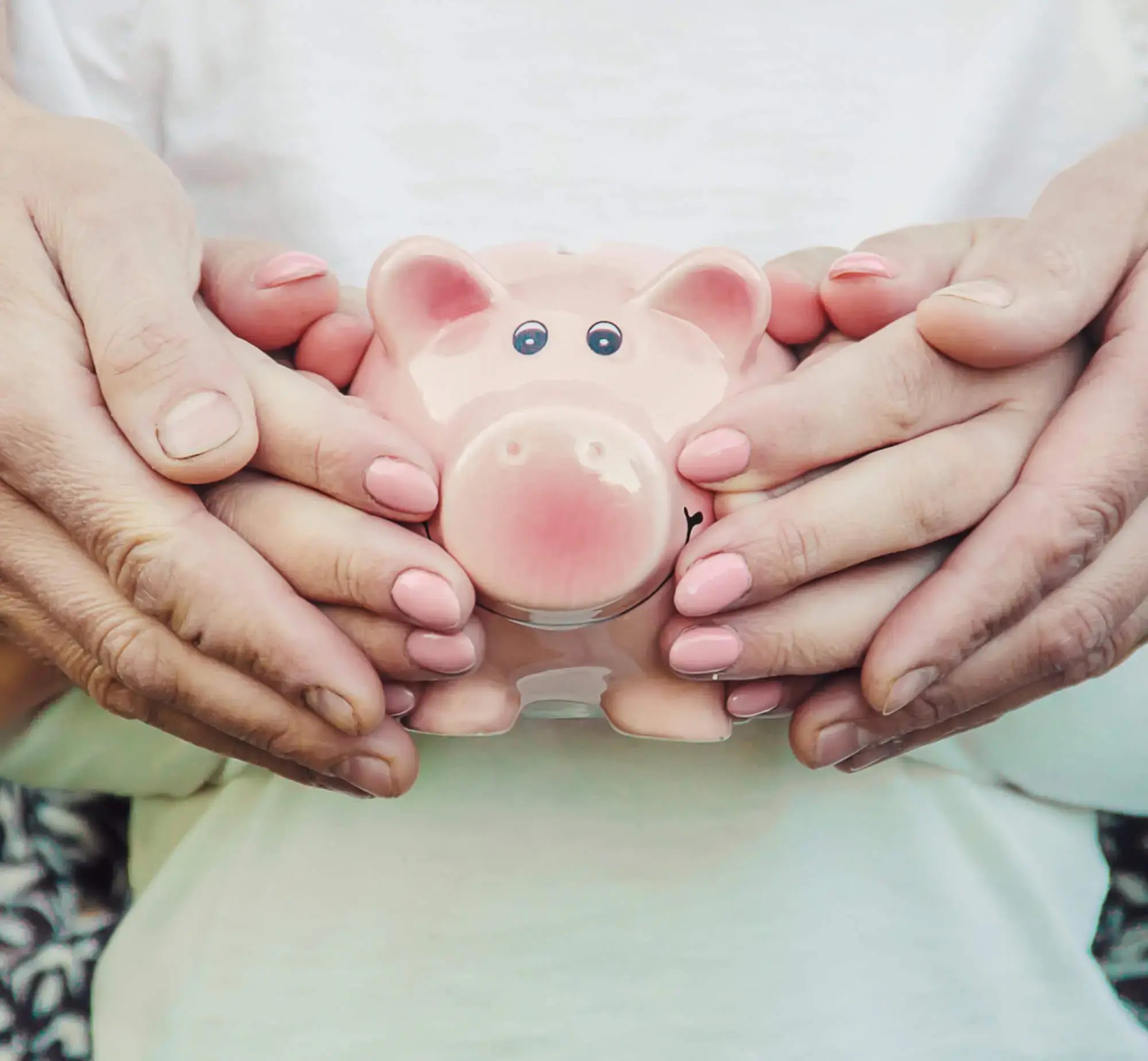Manos de un adulto y un niño sosteniendo juntos una alcancía rosada en forma de cerdito.
