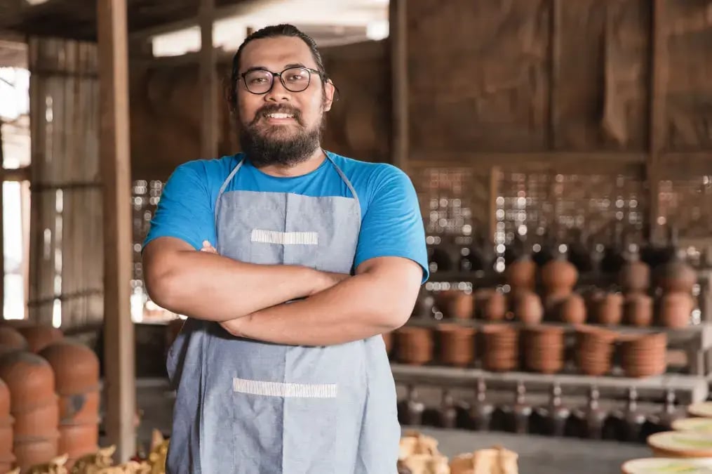 Hombre con delantal azul sonriendo en taller artesanal de cerámica.