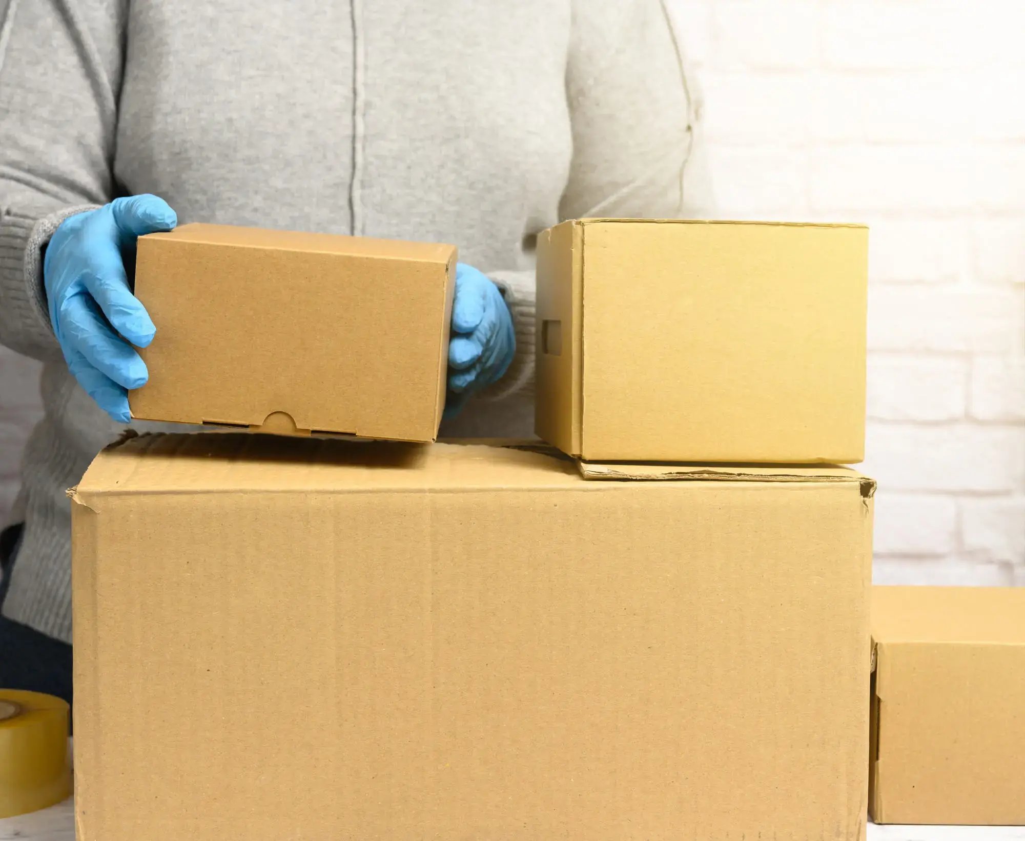 Persona con guantes azules sosteniendo una caja de cartón sobre otras cajas apiladas.