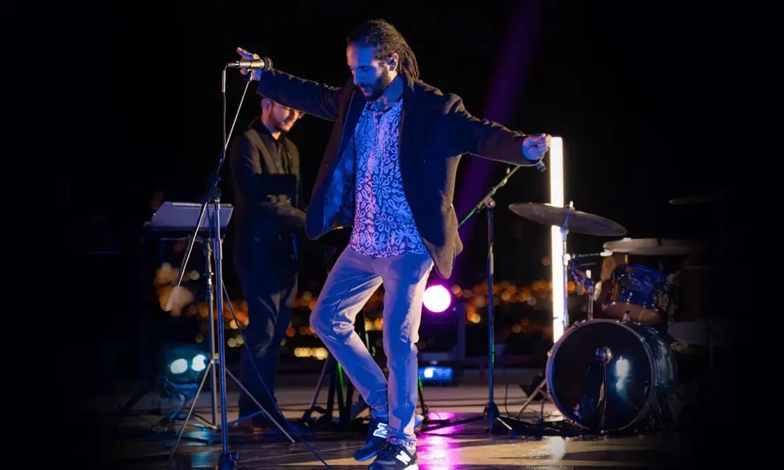 Músico cantando y bailando sobre el escenario durante un concierto nocturno con luces de colores.