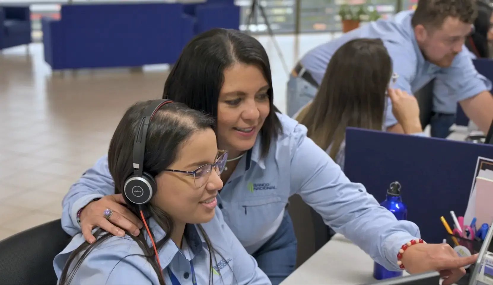 Empleada del Banco Nacional capacitando a otra colaboradora en una oficina.