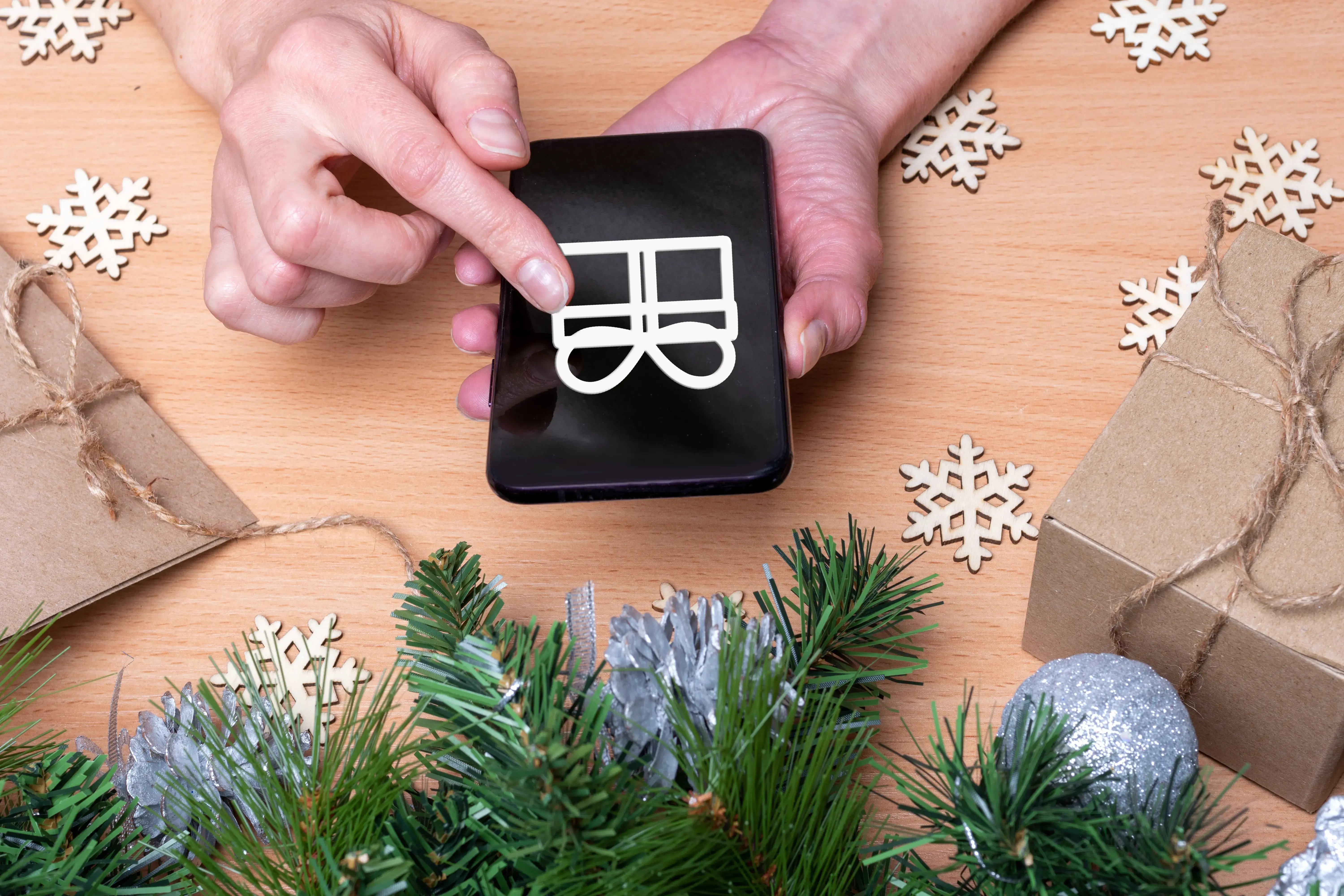 Persona utilizando un celular con ícono de regalo en la pantalla, rodeado de adornos y cajas navideñas.