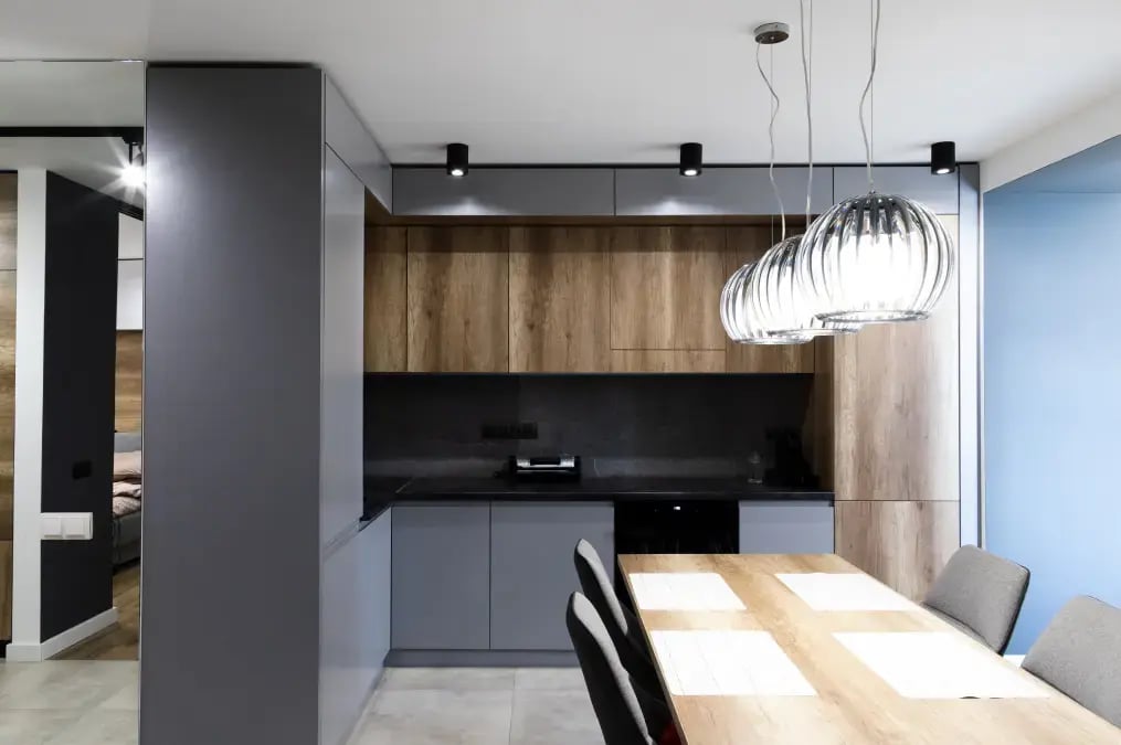 Cocina moderna con gabinetes de madera y grises, mesa de comedor y lámparas colgantes de diseño.