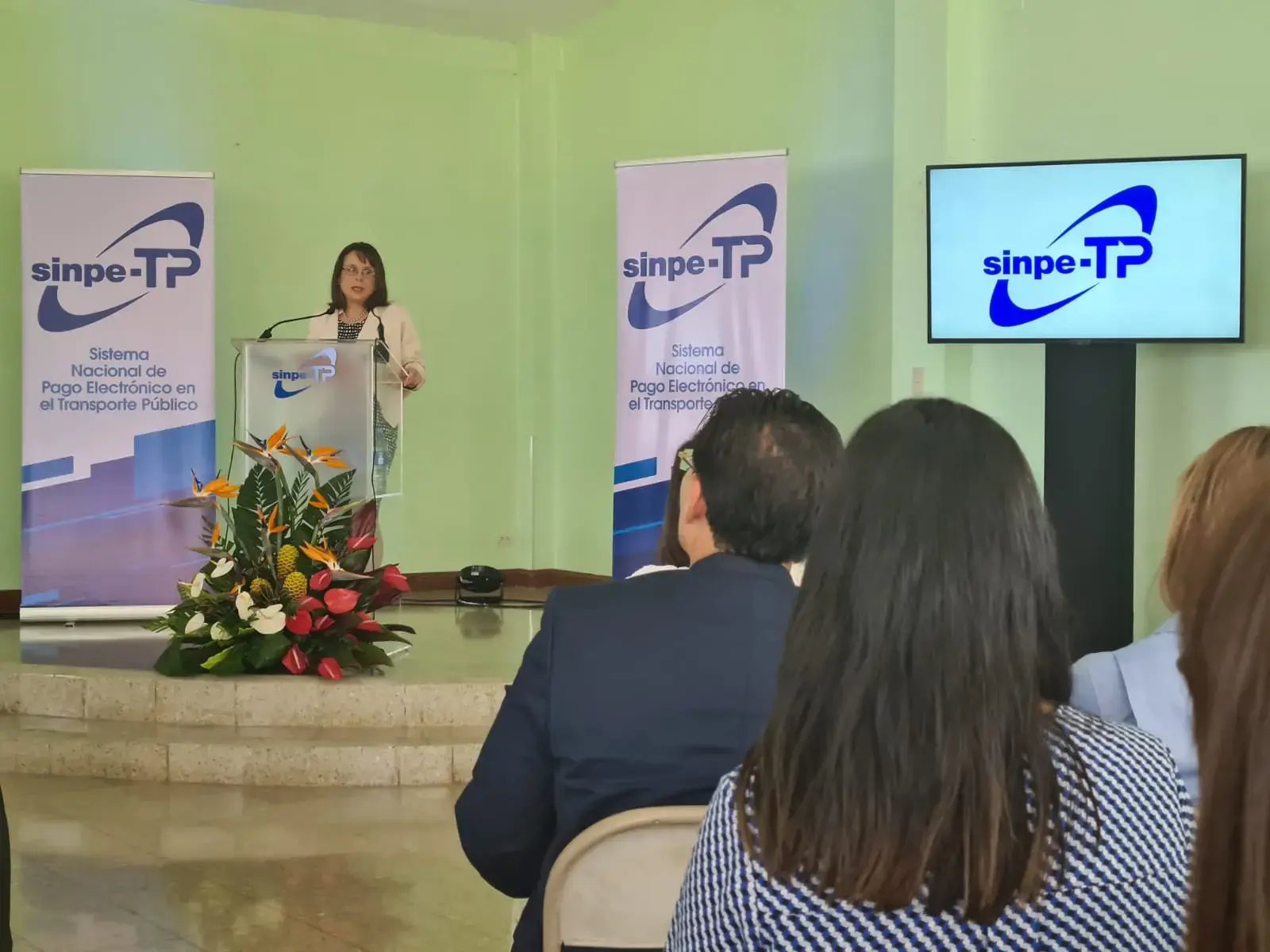 Mujer exponiendo en un podio durante una conferencia del sistema SINPE-TP en transporte público.