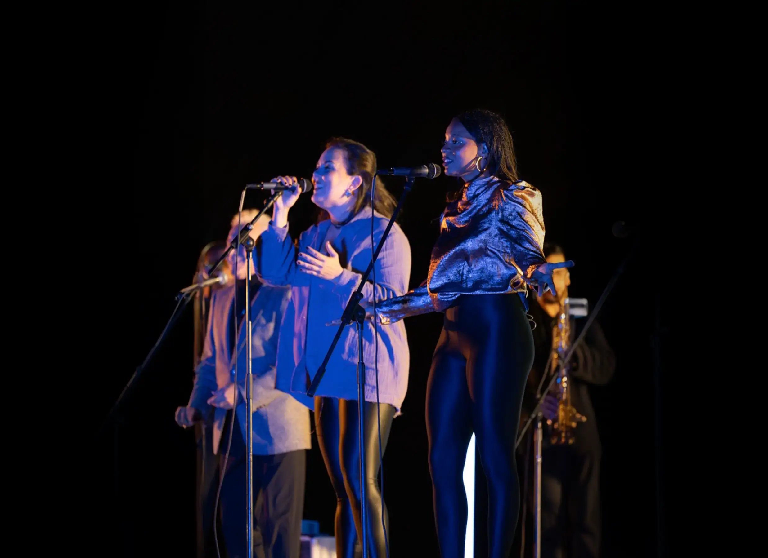 Coristas cantando en el escenario durante un concierto nocturno con iluminación azul.