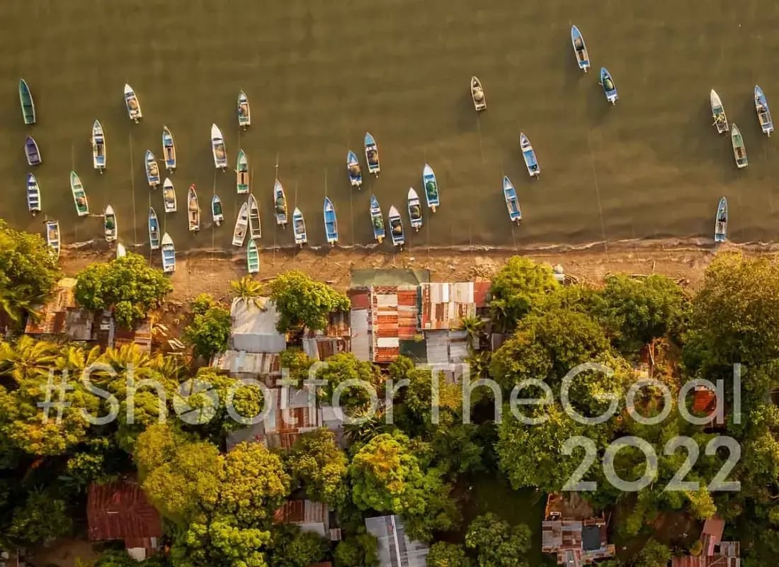 Vista aérea de botes alineados en la orilla de un río junto a una comunidad rodeada de árboles.