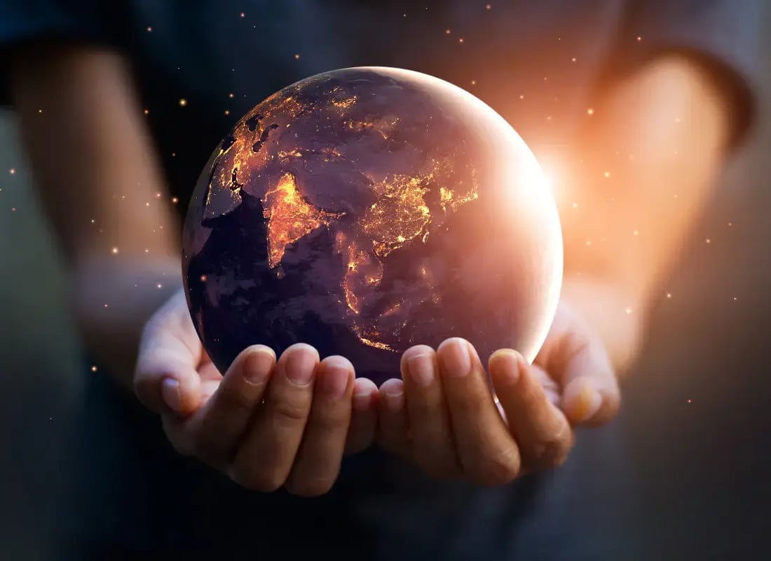 Manos sosteniendo un planeta Tierra iluminado con luces nocturnas de ciudades.