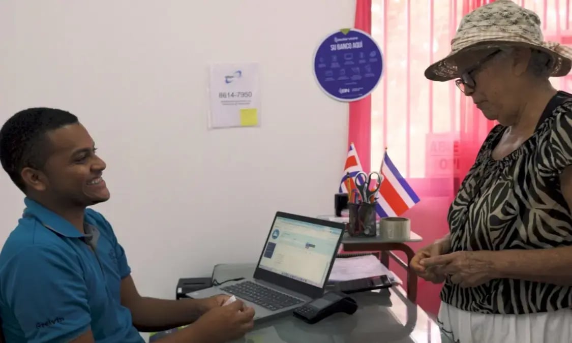 Empleado atendiendo a una mujer adulta mayor en oficina de BN Servicios