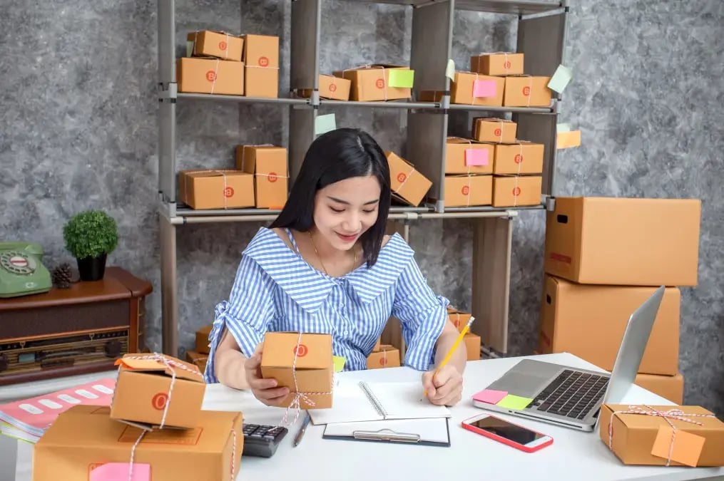 Mujer emprendedora trabajando en un negocio de ventas en línea, rodeada de cajas de envíos.