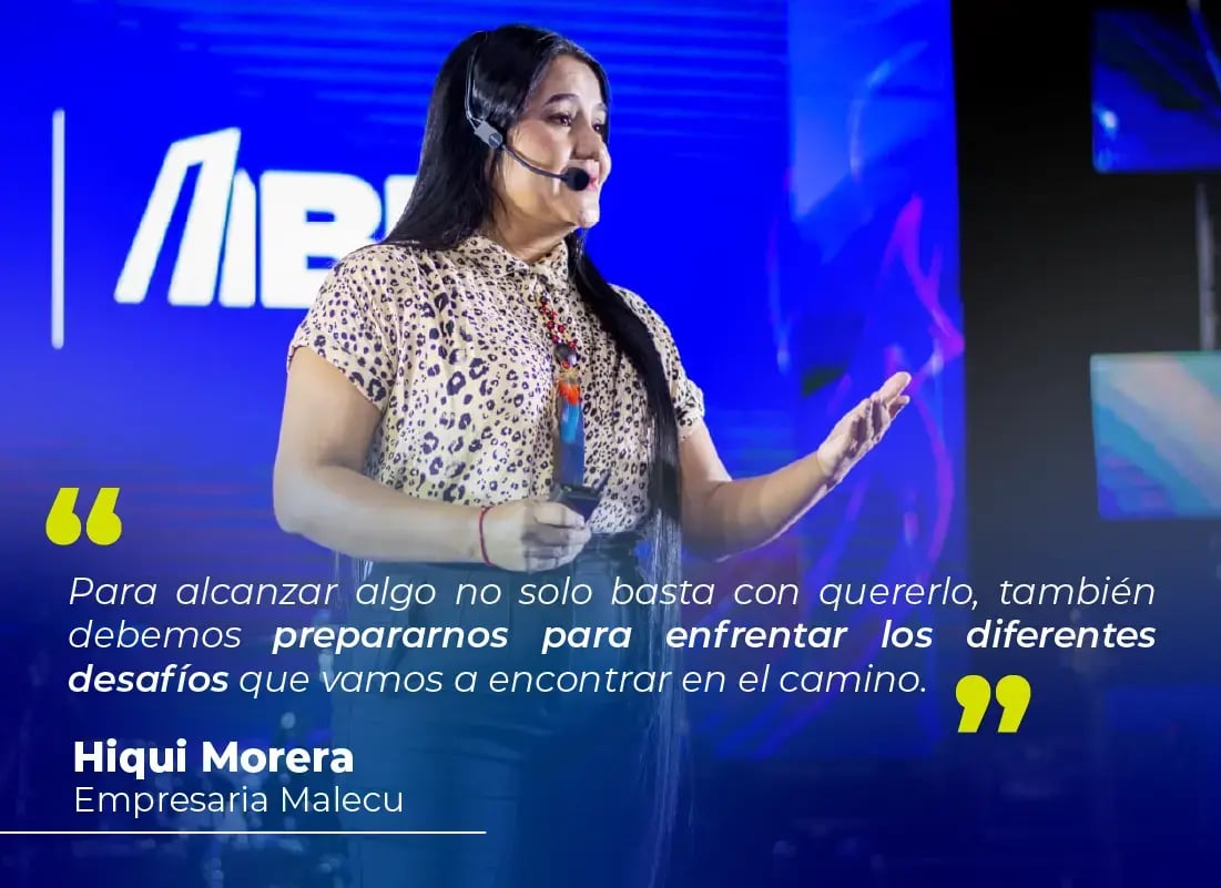 Mujer empresaria Malecu hablando en escenario con micrófono de diadema durante un evento del Banco Nacional, junto a una cita inspiradora proyectada.