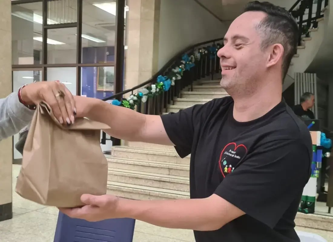 Hombre sonriente entrega una bolsa de papel durante una actividad en un espacio decorado con adornos navideños.