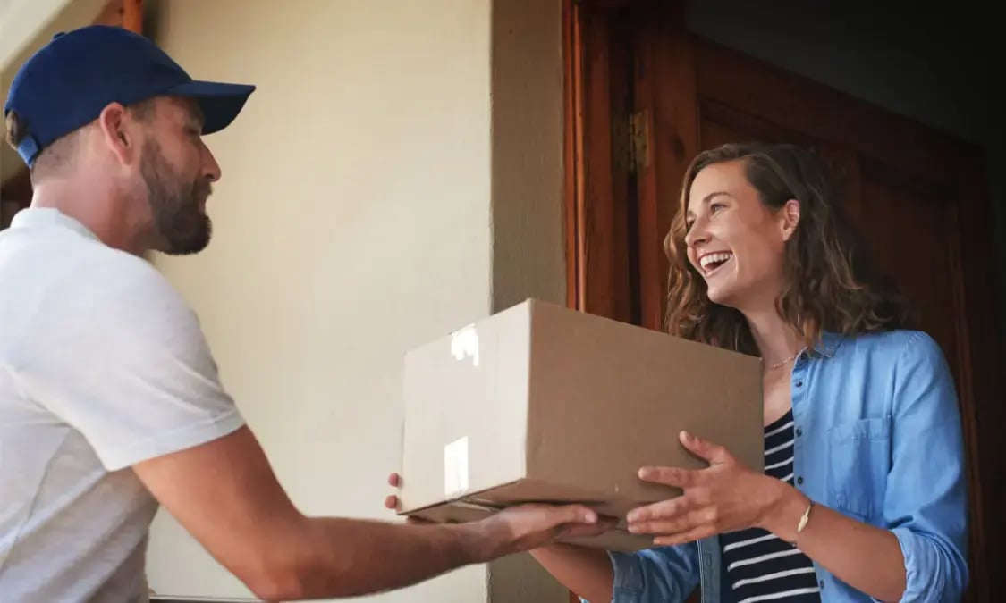 Mujer sonriente recibiendo un paquete de un repartidor en la puerta de su casa.