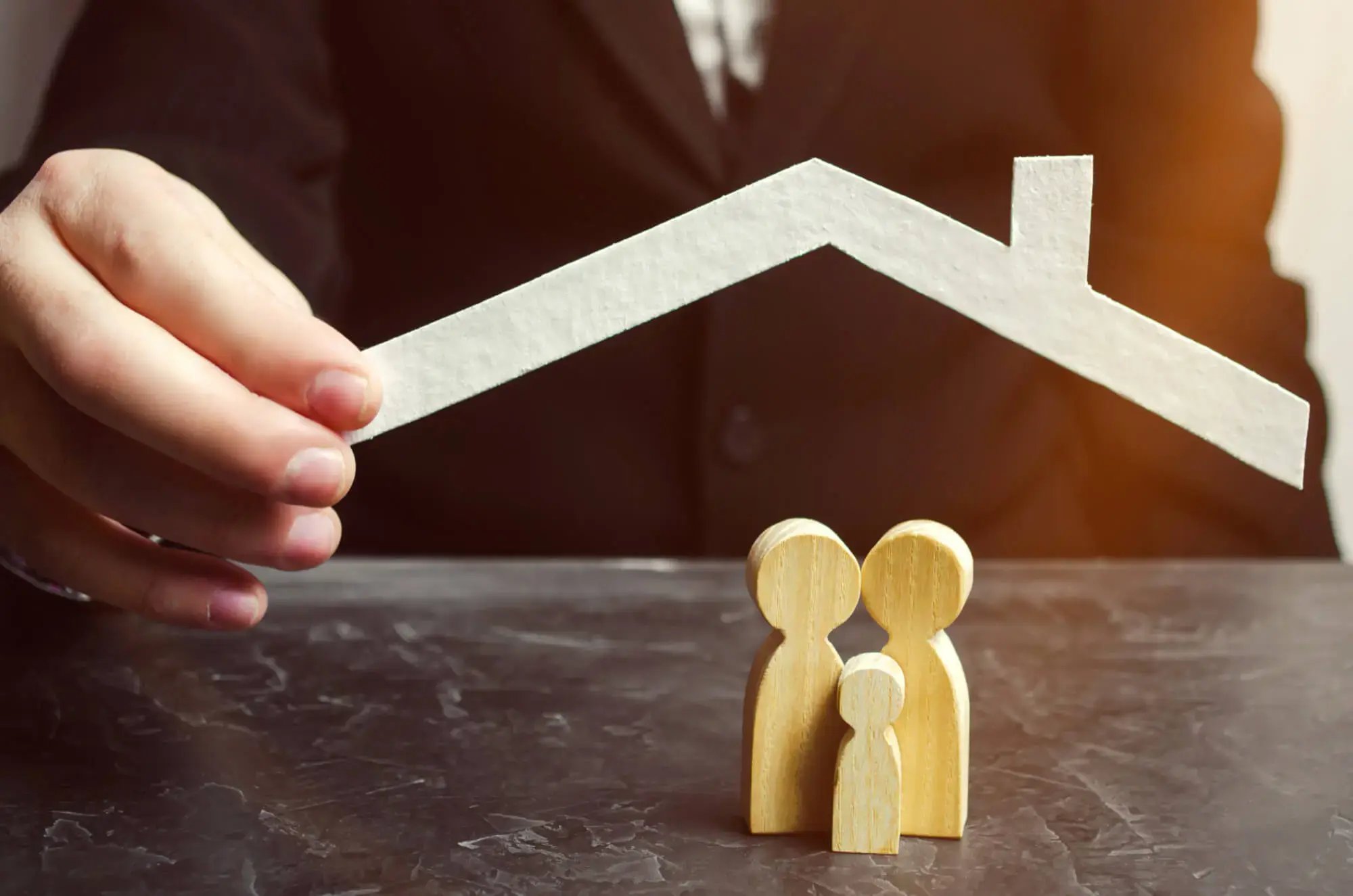 Mano colocando un techo de papel sobre figuras de madera que representan a una familia.