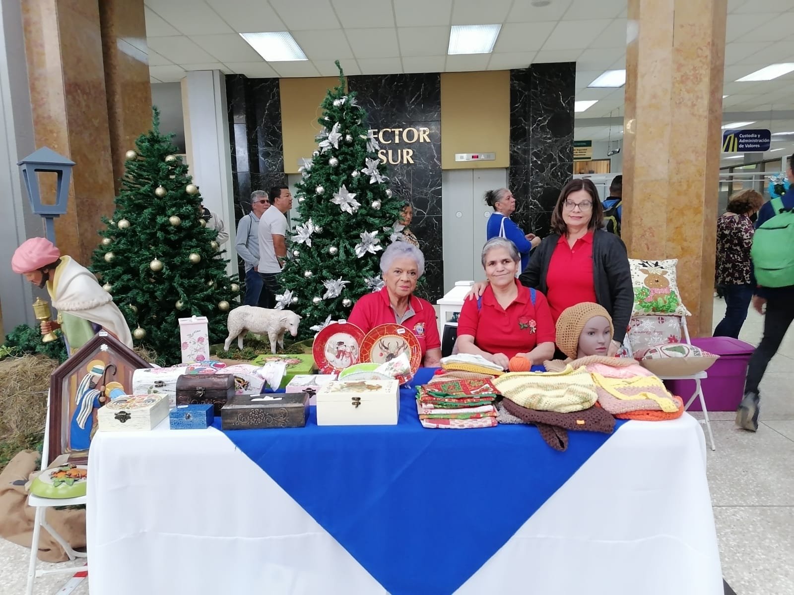 Grupo de mujeres adultas mayores presentan artesanías y tejidos en la feria navideña del Banco Nacional.