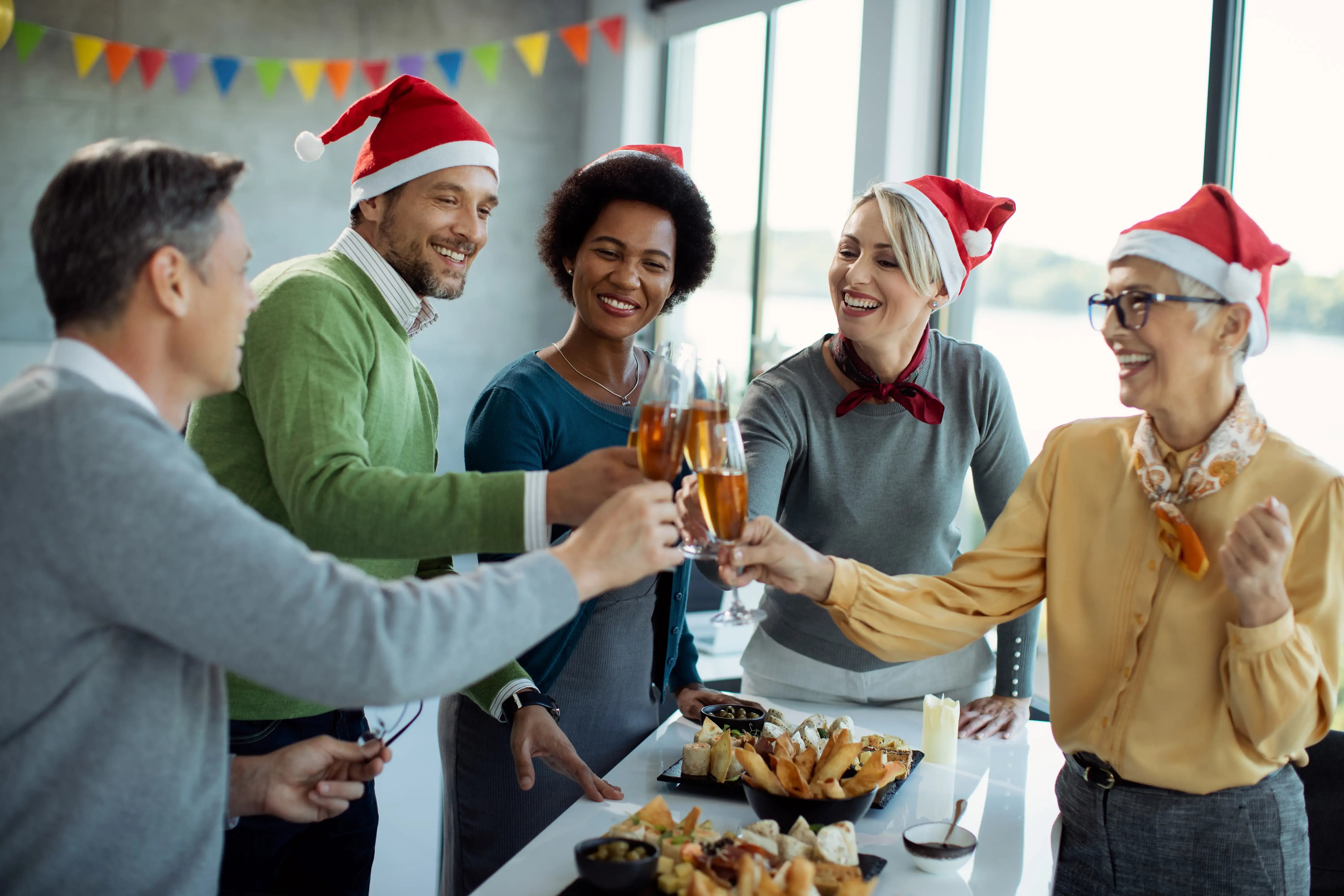 Grupo de compañeros celebrando en la oficina con gorros de Navidad y brindis festivo.
