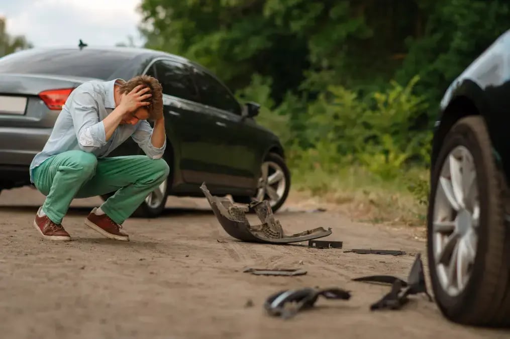 Hombre agachado con las manos en la cabeza tras un accidente de autos