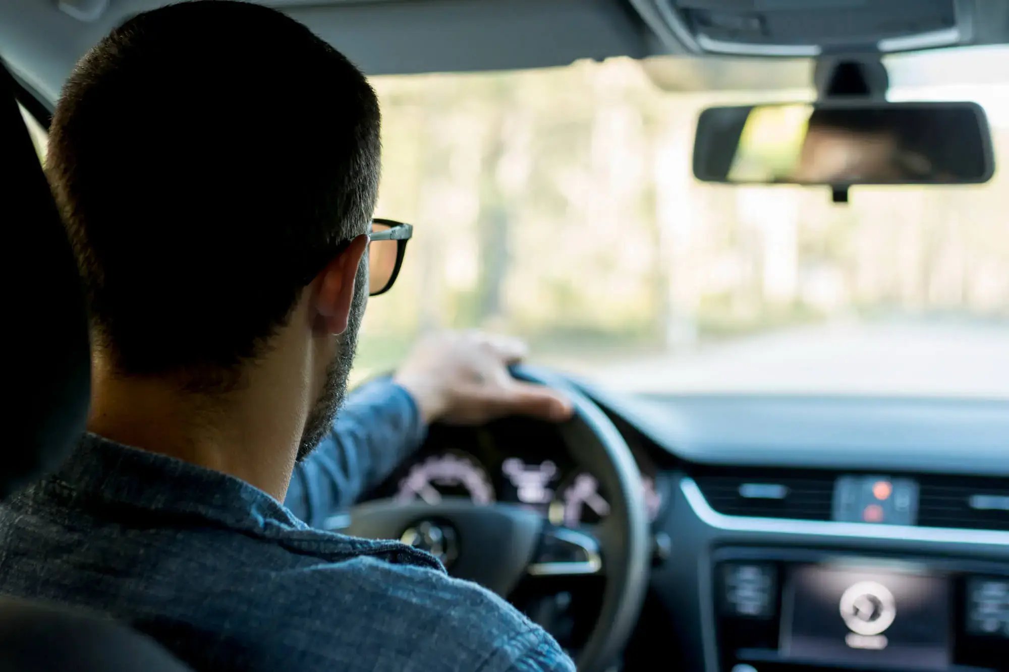 Hombre con gafas conduciendo un vehículo visto desde el asiento trasero.