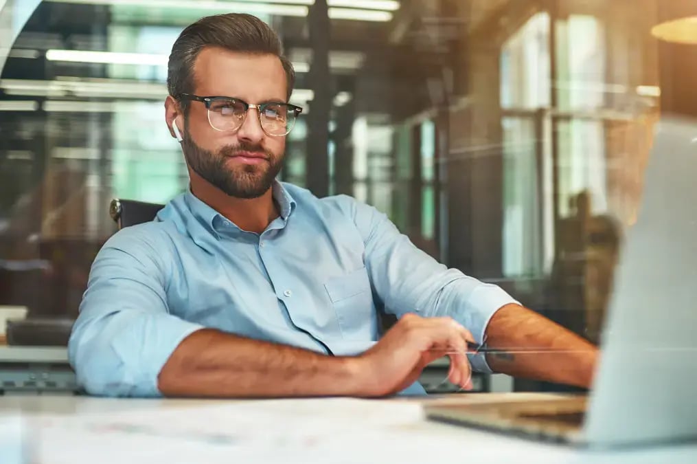 Hombre con gafas trabajando en una oficina frente a su computadora portátil.