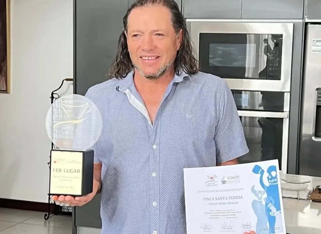 Hombre sosteniendo trofeo y certificado del primer lugar de la competencia Cup of Excellence Costa Rica