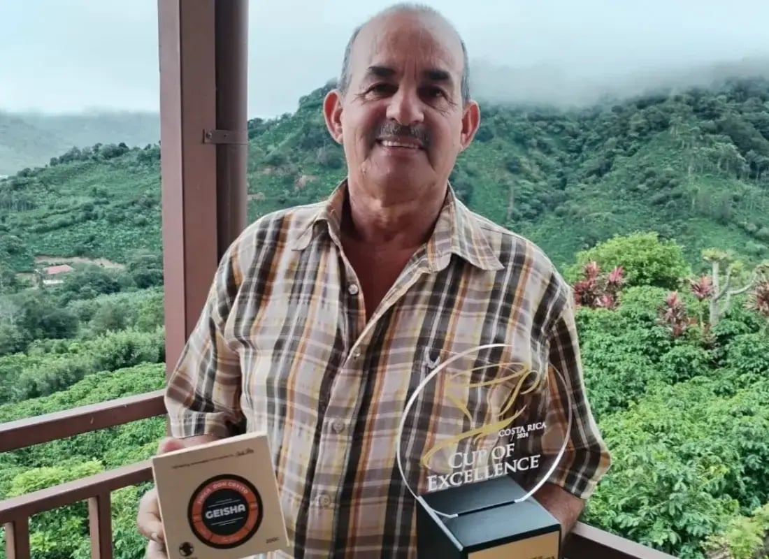 Productor de café sosteniendo un trofeo y una caja de café Geisha en una finca cafetalera