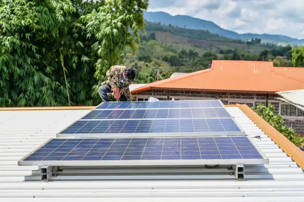 Técnico instalando paneles solares en el techo de una vivienda con paisaje de montaña.