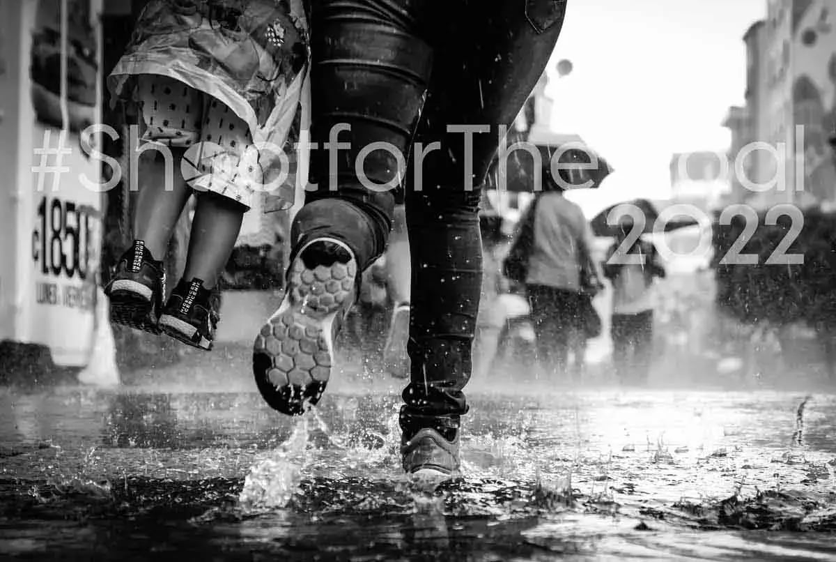 Personas caminando bajo la lluvia en una calle, con enfoque en los pies chapoteando en charcos.