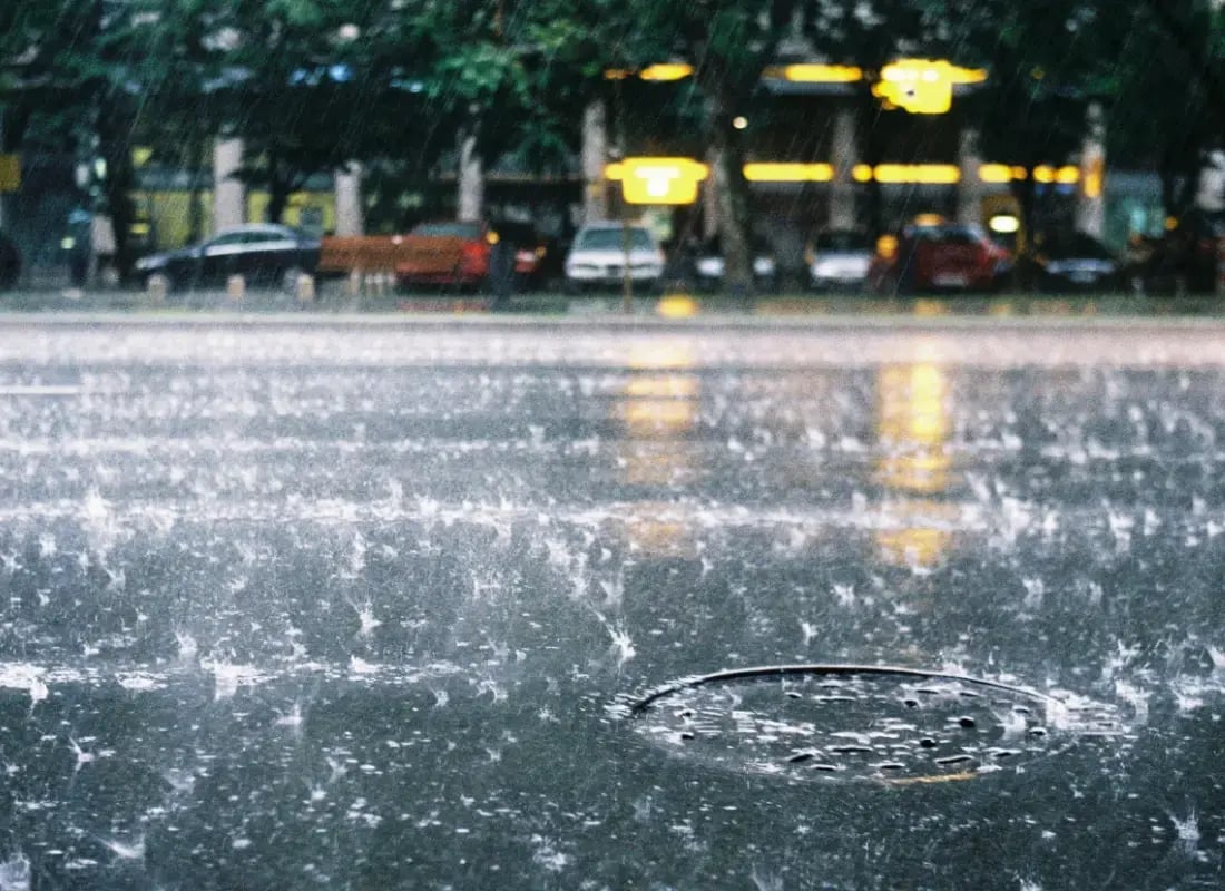 Lluvia intensa cayendo sobre una calle urbana con charcos y autos estacionados