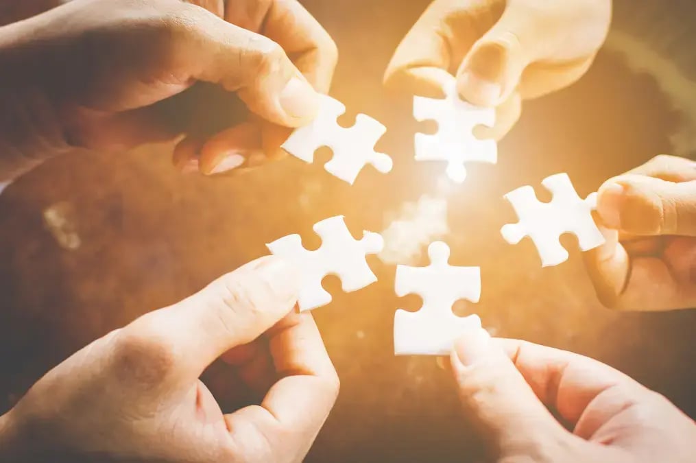Varias manos uniendo piezas de rompecabezas blancas sobre superficie marrón