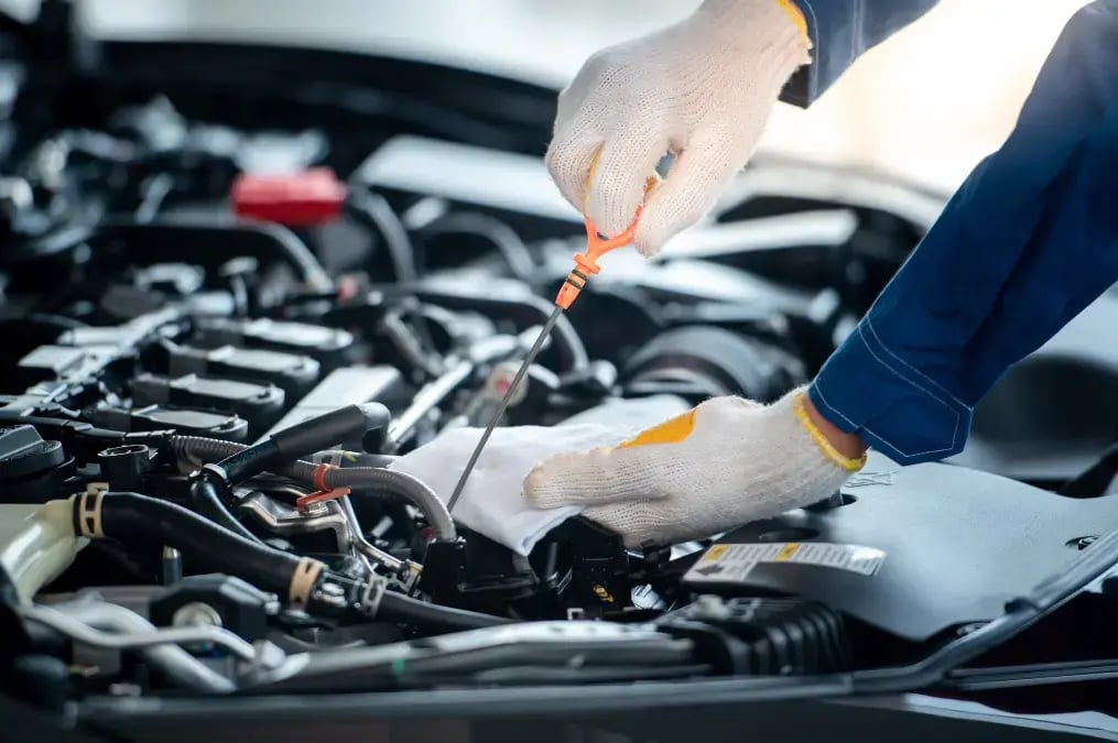 Mecánico revisando el aceite del motor de un automóvil con guantes de trabajo.