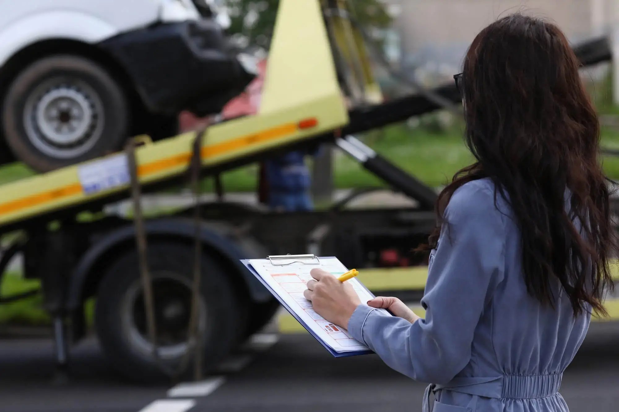 Mujer tomando notas en una libreta frente a un vehículo siendo remolcado.