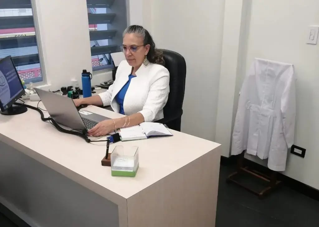 Mujer trabajando en oficina médica con computadora portátil.