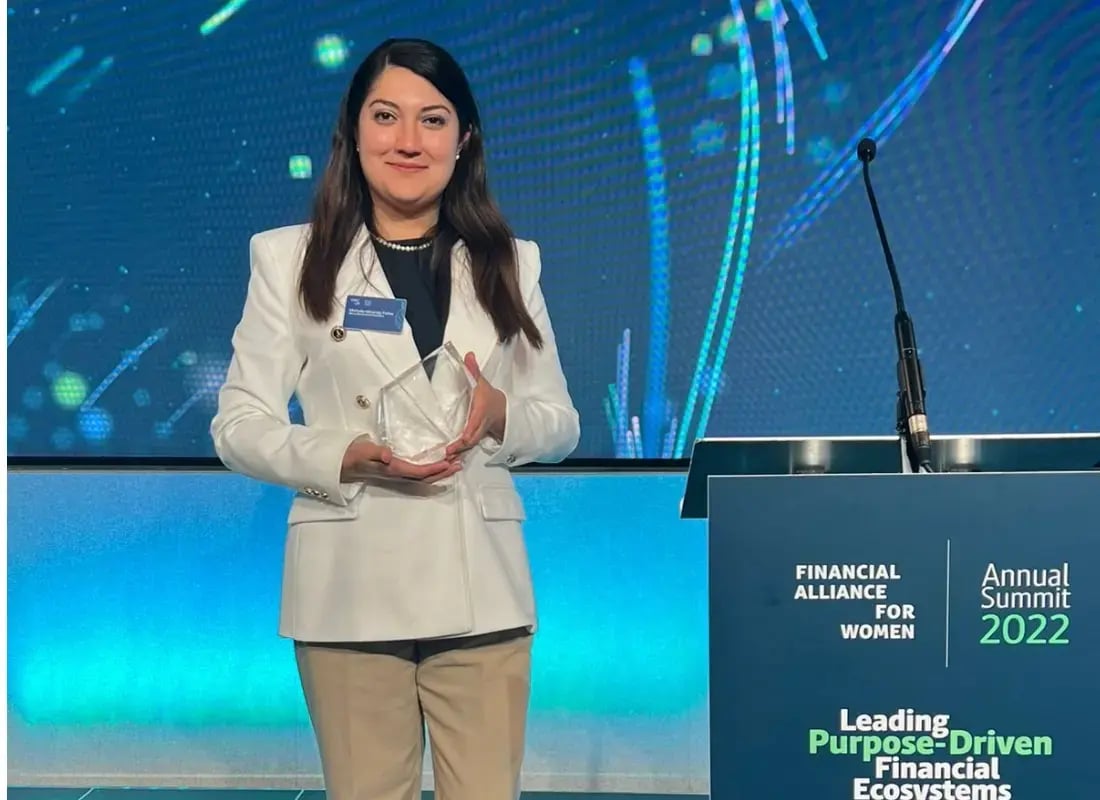 Mujer con saco blanco sosteniendo un trofeo de cristal en un escenario de premiación internacional.