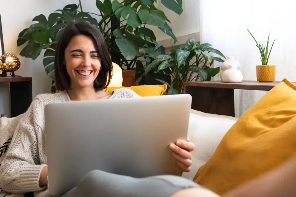 Mujer sonriente usando laptop en sala moderna con plantas decorativas