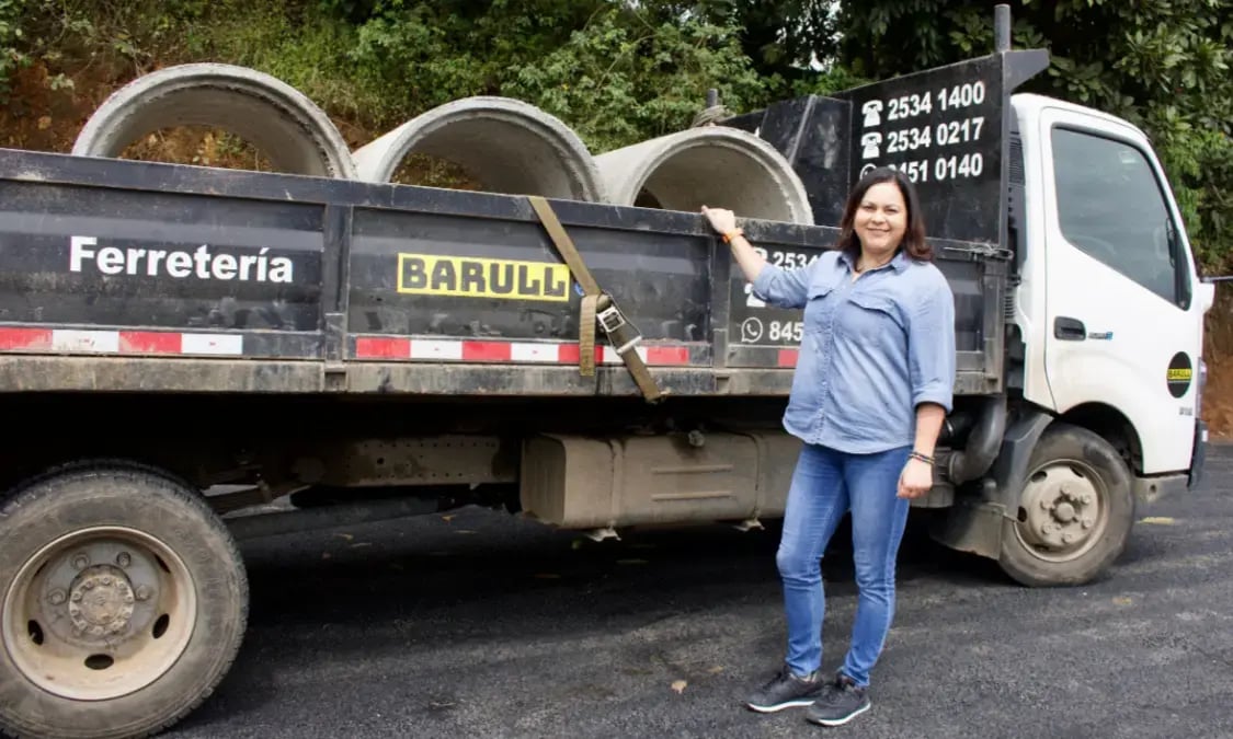 Mujer de pie junto a un camión de Ferretería Barulle cargado con tubos de concreto.