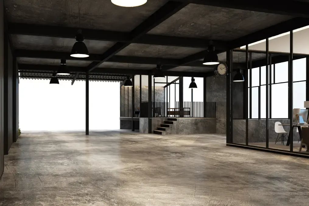 Espacio de oficina estilo industrial con paredes de concreto, lámparas colgantes y divisiones de vidrio.