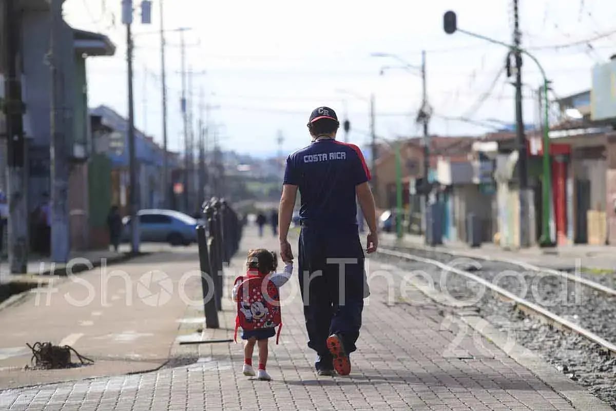 Hombre con camiseta de Costa Rica caminando de la mano con una niña por la vía del tren.