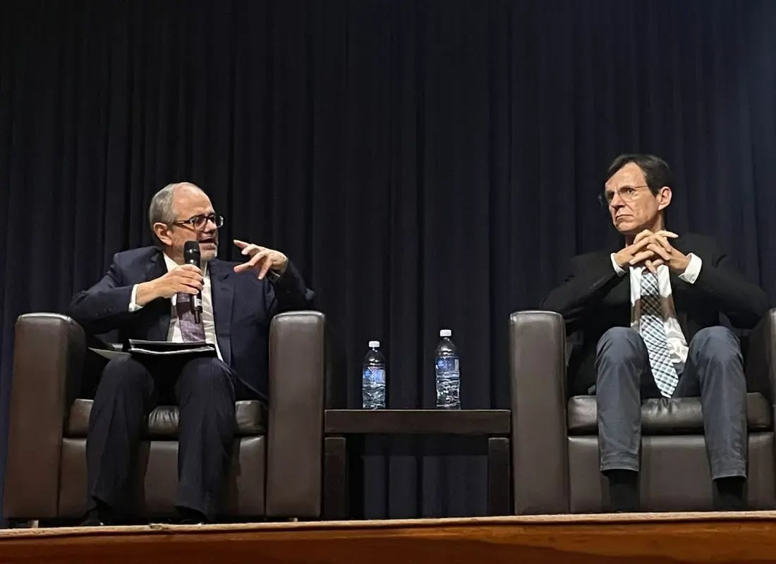 Dos panelistas sentados en sillones durante un debate en una conferencia.