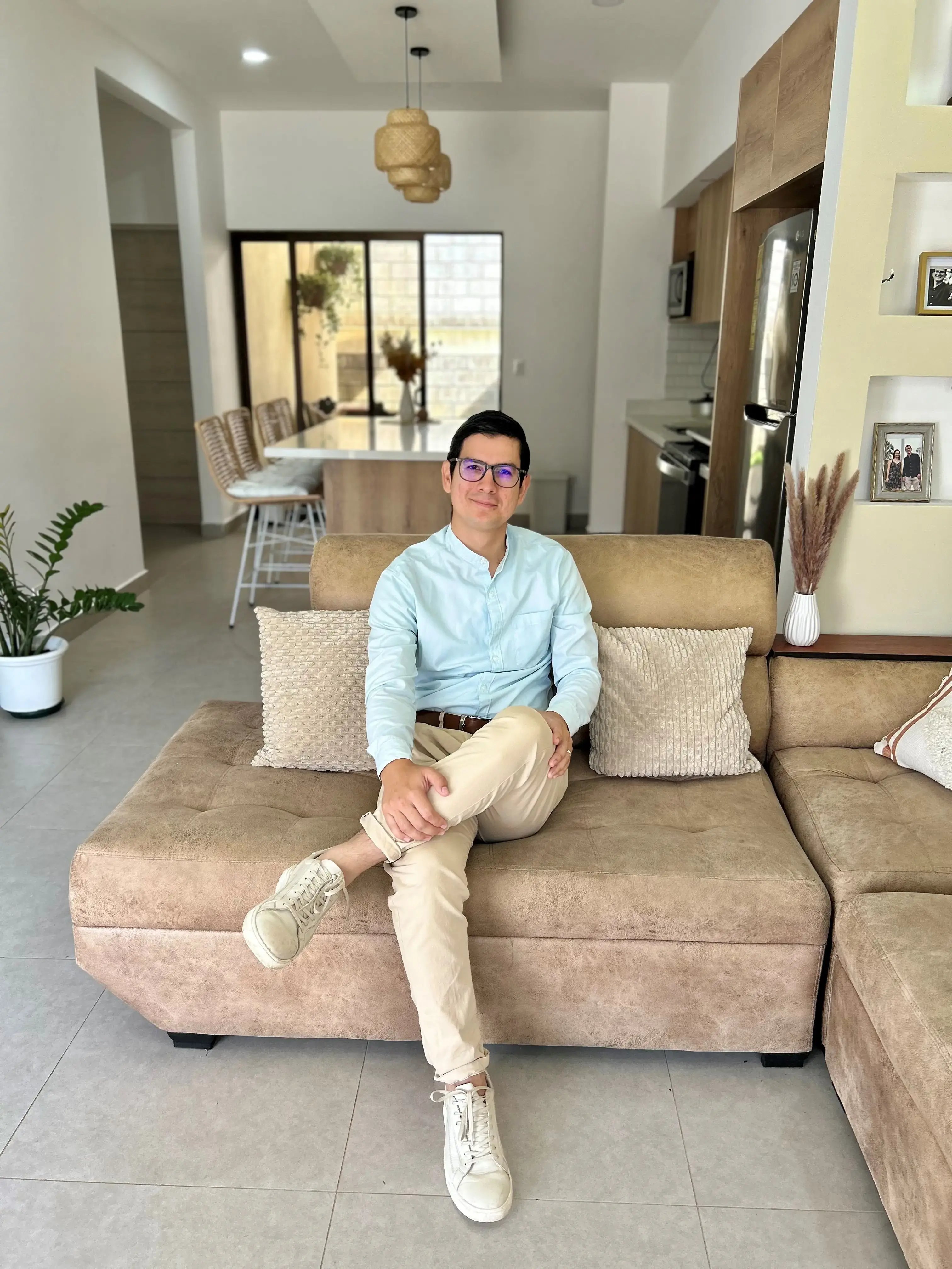 Persona sentada en un sillón beige dentro de una sala moderna con cocina al fondo y decoración minimalista.