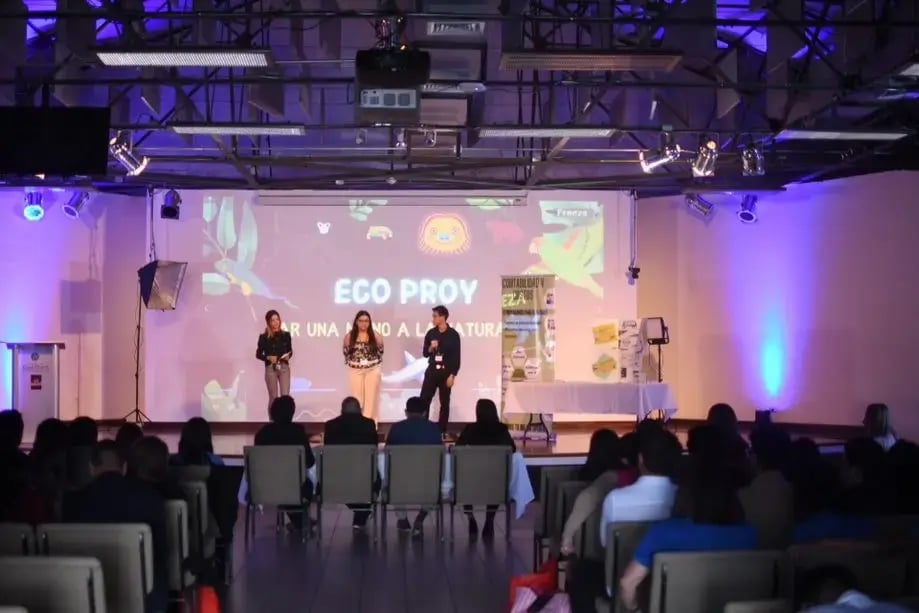 Expositores presentando un proyecto ambiental llamado Eco Proy en un escenario con público.