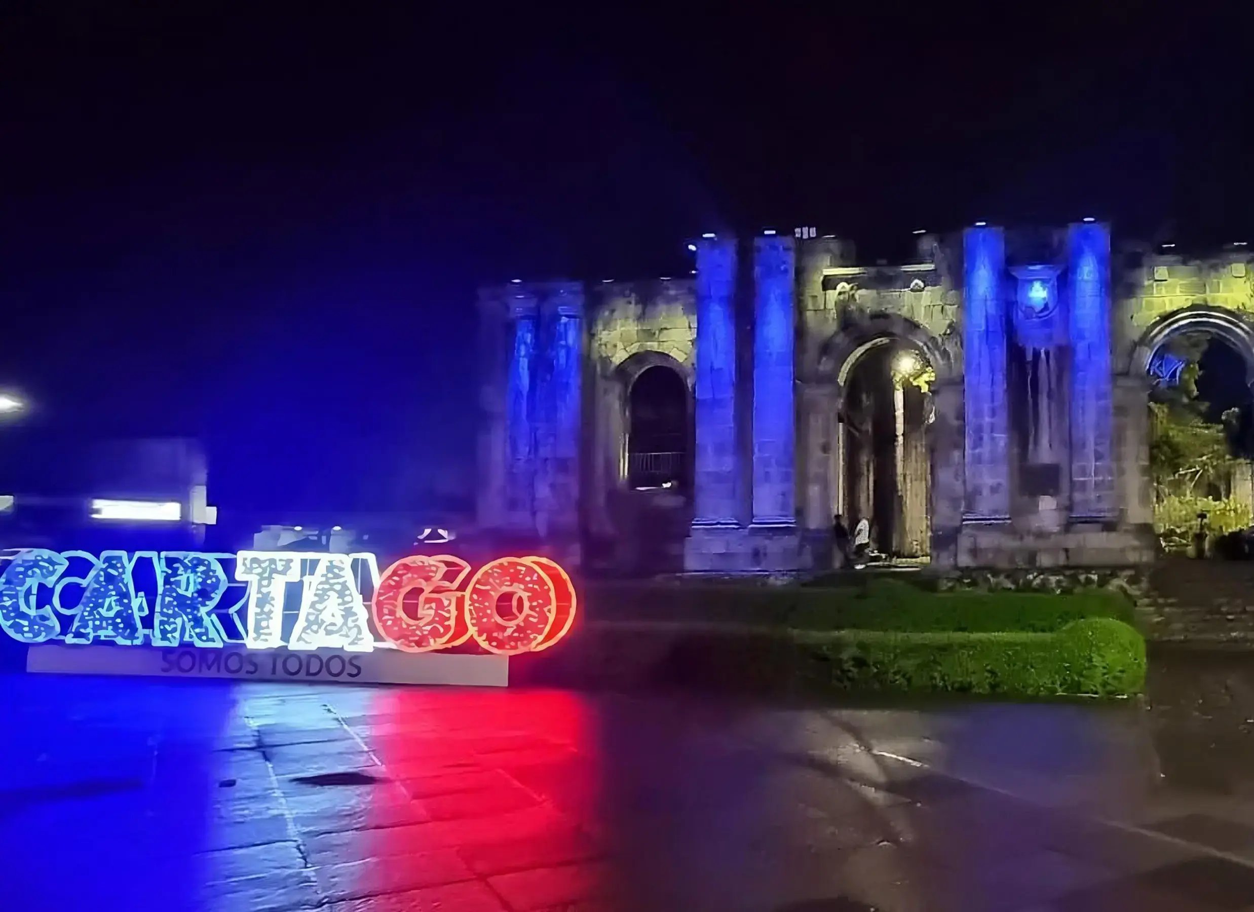 Ruinas de la Parroquia de Santiago Apóstol en Cartago iluminadas de azul durante la noche con el letrero “Cartago somos todos” al frente.