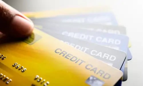 Mano sostiene varias tarjetas de crédito en abanico, destacando una tarjeta amarilla al frente.