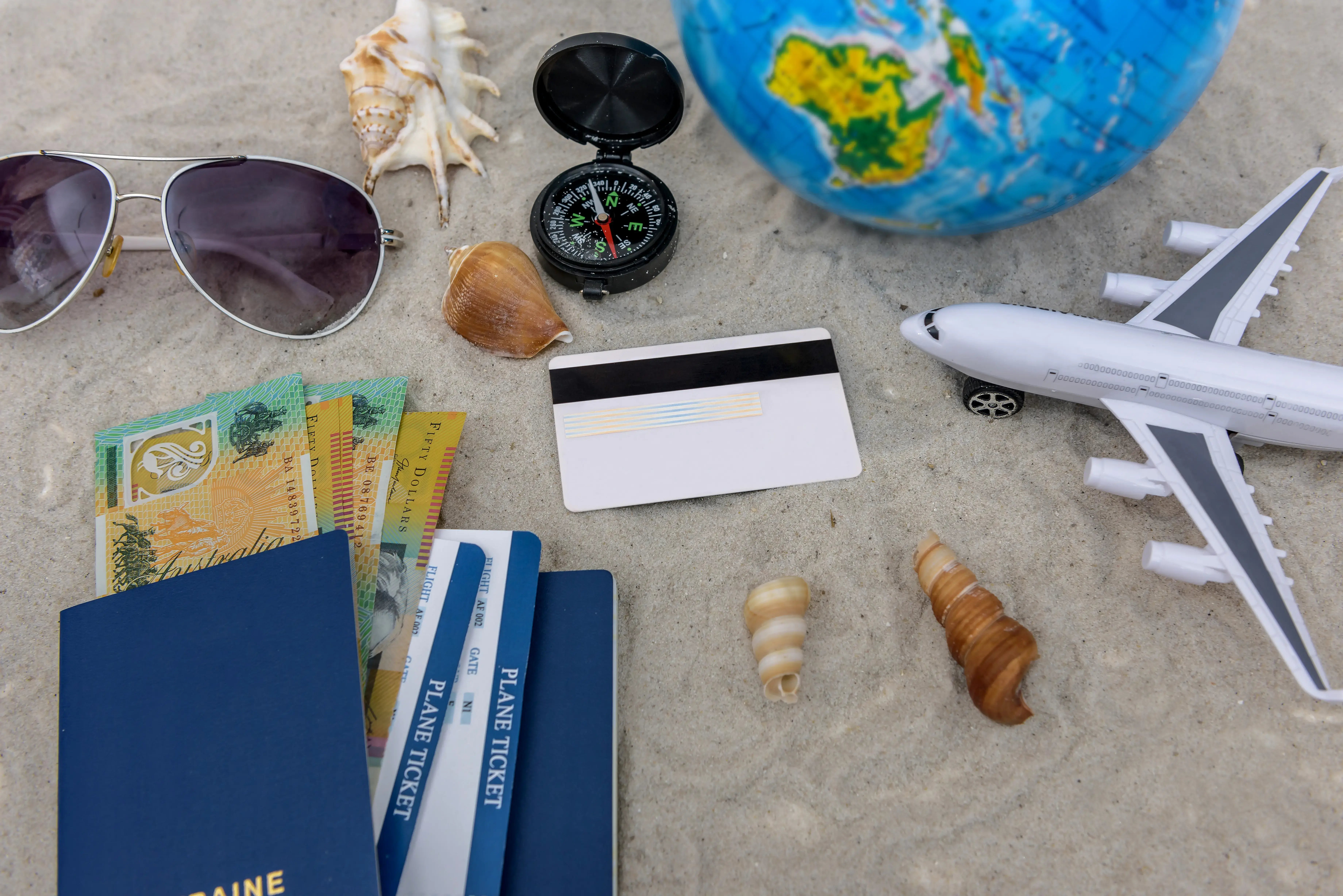 Pasaporte, boletos de avión, dinero y tarjeta sobre arena con elementos de viaje, Banco Nacional de Costa Rica BNCR.