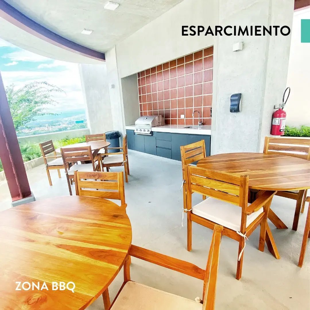Área social con mesas de madera y parrilla en zona BBQ del condominio