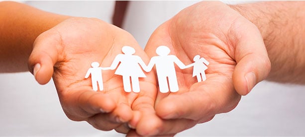 Persona adulta sosteniendo figuras de papel que representan una familia, simbolizando protección y bienestar familiar.